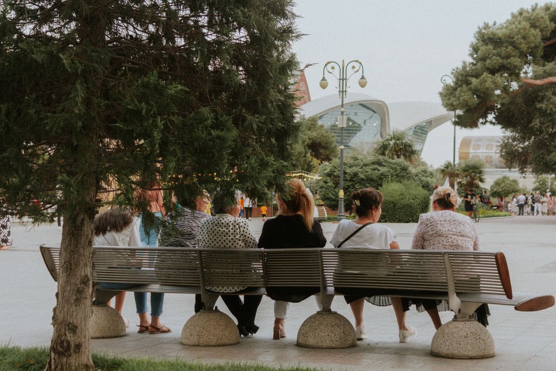 Personas descansando en una banca junto a una plaza urbana moderna